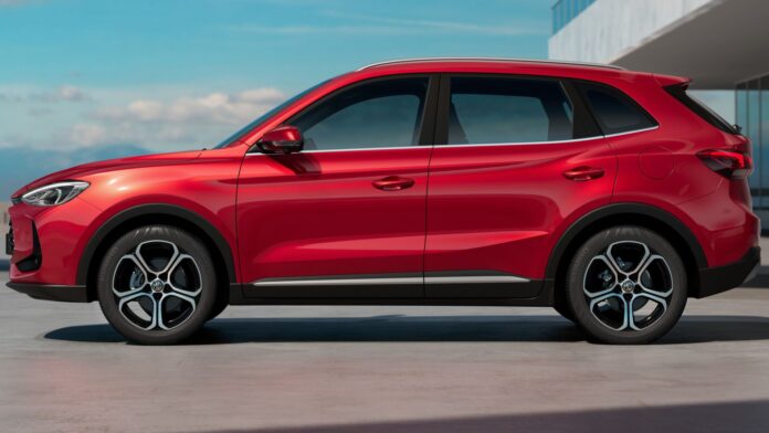 Czerwony SUV MG HS prezentuje profil nadwozia na tle nowoczesnej architektury