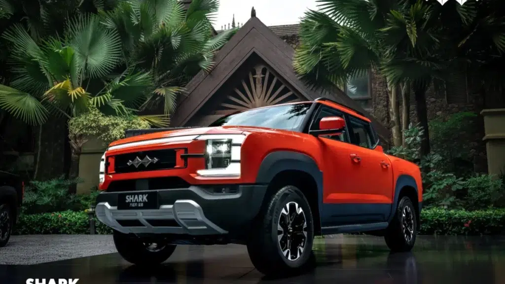 Pomarańczowy pickup BYD Shark zaparkowany przed nowoczesnym budynkiem w otoczeniu palm